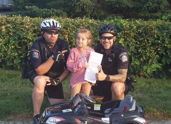 Two Saint-Jérôme police officers pose with six-year-old Mélodie Cherkezian after jokingly writing her up for using her phone while driving.