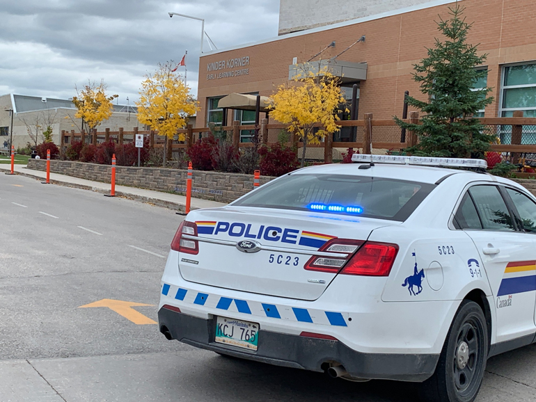 A white RCMP cruiser is parked outside a brick building.