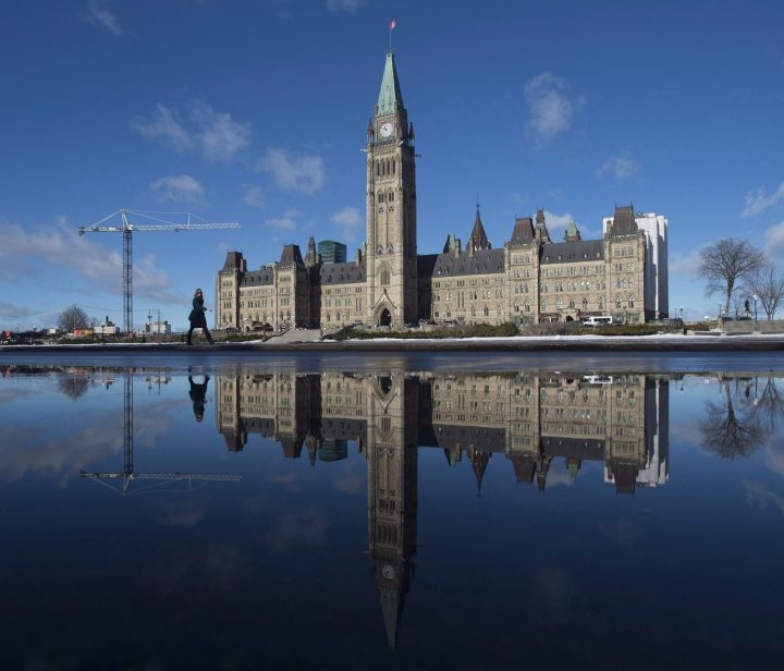 The centre block of the Parliament buildings is reflected in a puddle as a women walks past, Monday February 1, 2016 in Ottawa. A Saskatchewan man accused of threatening to shoot Prime Minister Justin Trudeau and blow up the Parliament buildings has been acquitted.David Petersen, 53, faced a charge of uttering threats after police said he made the threats over the phone to a government worker. 