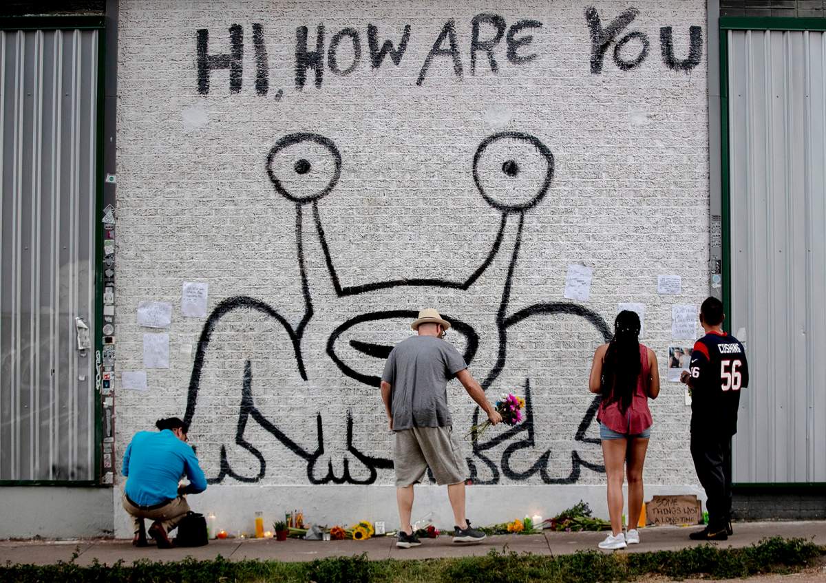 A man places flowers beneath the “Hi, How Are You” mural created by artist Daniel Johnston on Sept. 11, 2019, in Austin, Texas.