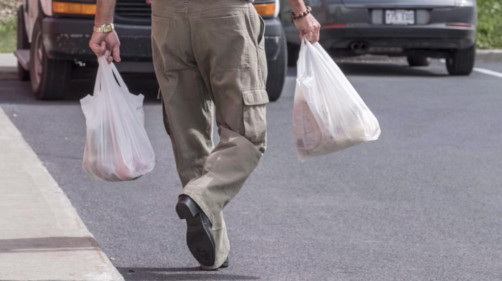 A shopper leaves a grocery store carrying his groceries in plastic bags in Brossard, Que. on August 30, 2016.