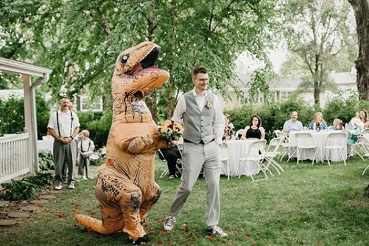 Christina Meador is shown in a dinosaur suit alongside a groomsman at her sister‘s wedding in Omaha, Neb., on Aug. 10, 2019.