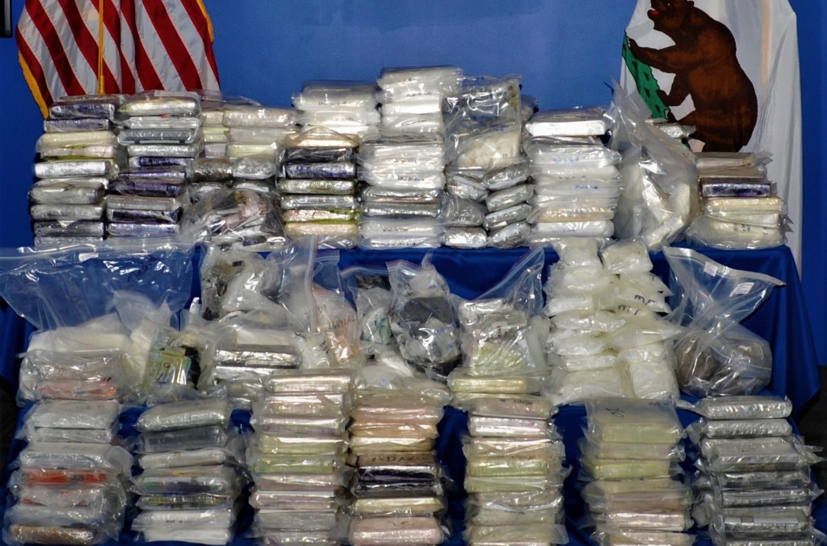 Hundreds of packages of illegal drugs are piled in front of U.S. and California state flags in an undated photo, the result of police busting a major drug trafficking ring that operated in B.C. and California.