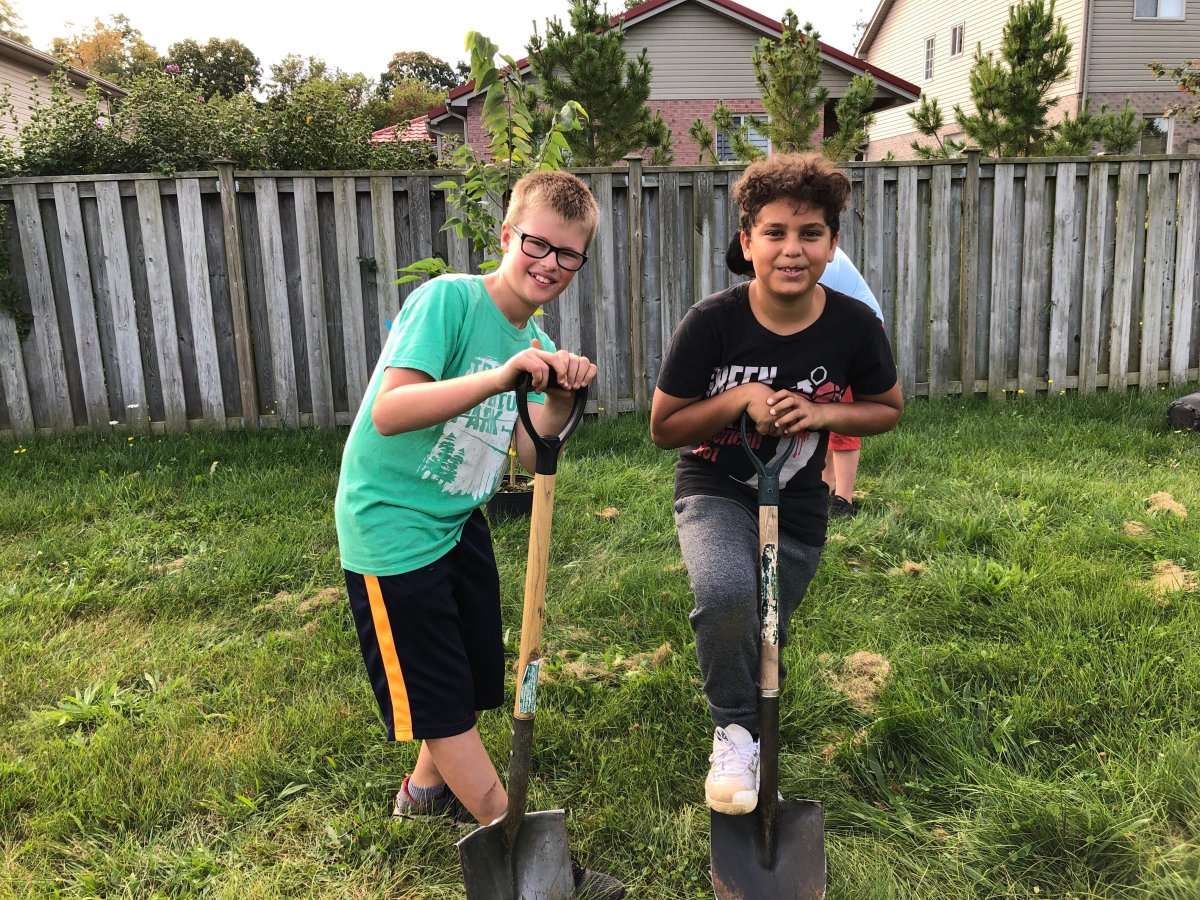 Sixth graders Finn, left, and Khallid pose with their shovels during a tree planting event at Kilally Meadows Environmentally Significant Area.