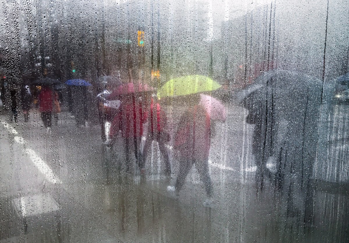 Pedestrians carrying umbrellas to shield themselves from the rain are seen through a cafe window covered with rain and steam in Vancouver, B.C., on March 11, 2017. 