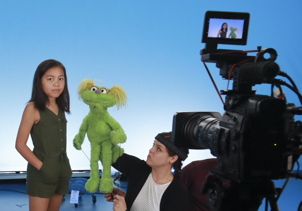 Salia Woodbury, 10, left, from Irvine, Calif., on the set with ‘Sesame Street’ muppet Karli and puppeteer Haley Jenkins during a taping about parental addiction in New York. Sesame Workshop is addressing the issue of addiction. (AP Photo/Bebeto Matthews)