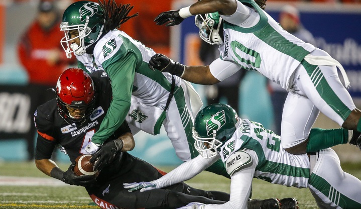 Saskatchewan Roughriders' Ed Gainey, top, left, Loucheiz Purifoy, centre, and Solomon Elimimian, top right, bring down Calgary Stampeders' Eric Rogers during second half CFL football action in Calgary, Oct. 11, 2019.