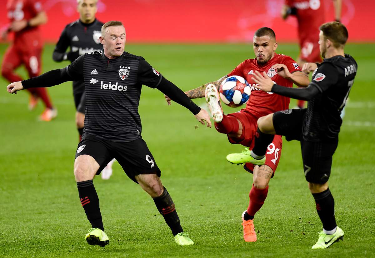 Toronto FC defender Auro (96) receives the ball under pressure from D.C. United forward Wayne Rooney (9) and teammate Paul Arriola (7) during second half MLS playoff soccer action in Toronto on Saturday, Oct. 19, 2019.