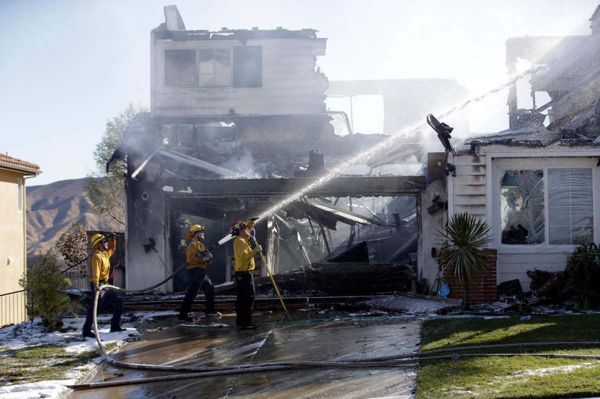 Firefighters try to put out a residence fire caused by a wildfire Friday, Oct. 25, 2019, in Santa Clarita, Calif.