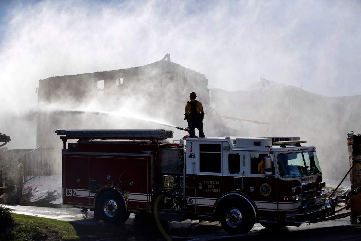 A firefighter tries to put out a residence fire caused by a wildfire from atop a fire truck Friday, Oct. 25, 2019, in Santa Clarita, Calif.