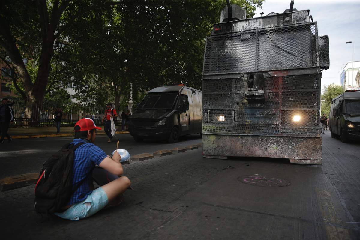 A man sits in front of Police tanks during protests against the Government, in Santiago, Chile, 26 October 2019.