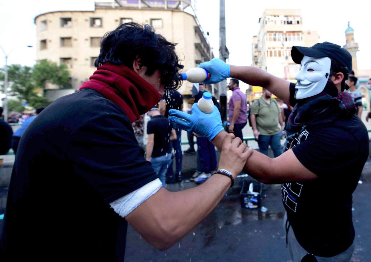 An Iraqi protester wearing mask helps a man after being affected by tear gas, which was dispensed by riot police during clashes with protesters at al-Tahrir square, central Baghdad, Iraq, 27 October 2019.