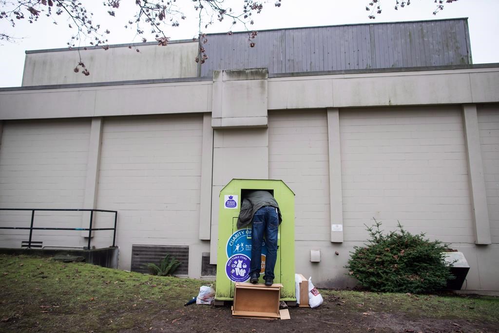 A man tries to retrieve items from a clothing donation bin in Vancouver, on Wednesday December 12, 2018. Clothing donation bins can return to the streets of Vancouver, as long as they meet a strict set of conditions. A statement from the City of Vancouver says councillors have approved new rules covering bins on city and private property. THE CANADIAN PRESS/Darryl Dyck