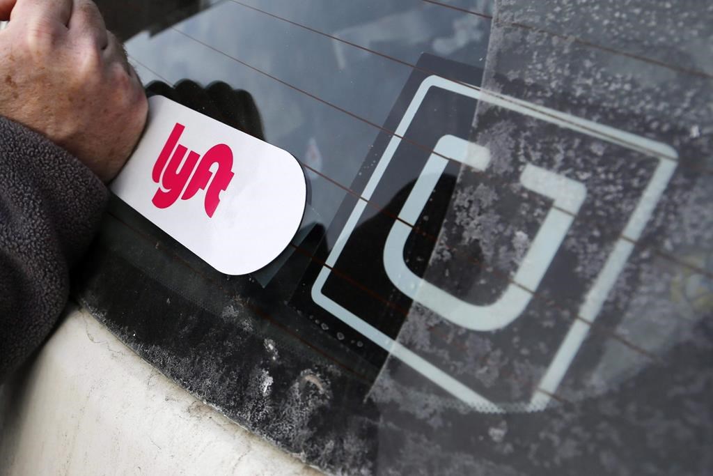 In this Jan. 31, 2018, file photo, a Lyft logo is installed on a Lyft driver's car next to an Uber sticker in Pittsburgh.