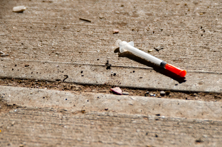 A discarded needle lays on a sidewalk.