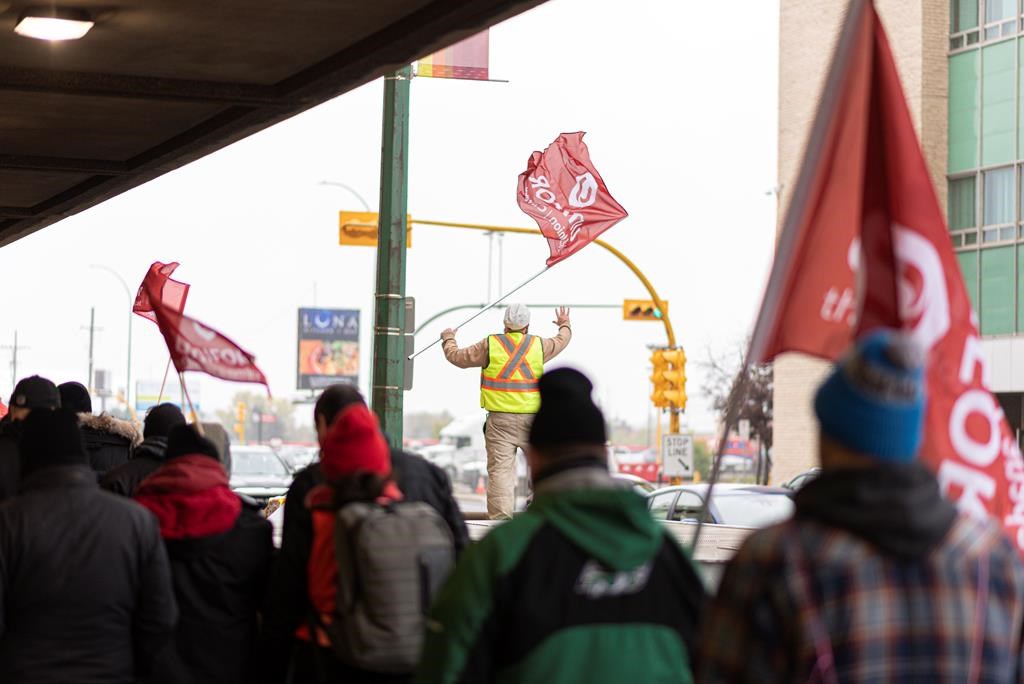 SaskTel employee Ryan Cleniuk, centre, waves to drivers in the hope of a supportive "honk" near a SaskTel building on Saskatchewan Drive in downtown Regina on Friday, Oct. 4, 2019.
