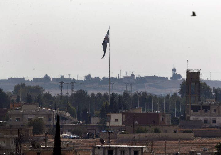 In this Oct. 22, 2019 photo taken from the Turkish side of the border between Turkey and Syria, in Akcakale, Sanliurfa province, southeastern Turkey, Syria's opposition flag flies on a pole in Tal Abyad, Syria. 