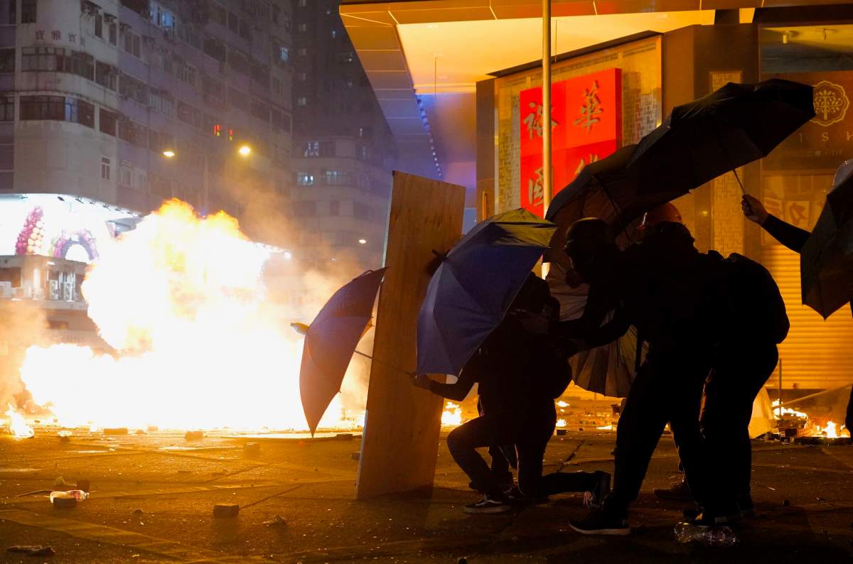 Protesters take cover with umbrellas from tear gas canisters in the Kowloon area of Hong Kong, Monday, Nov. 18, 2019. (AP Photo/Vincent Yu)