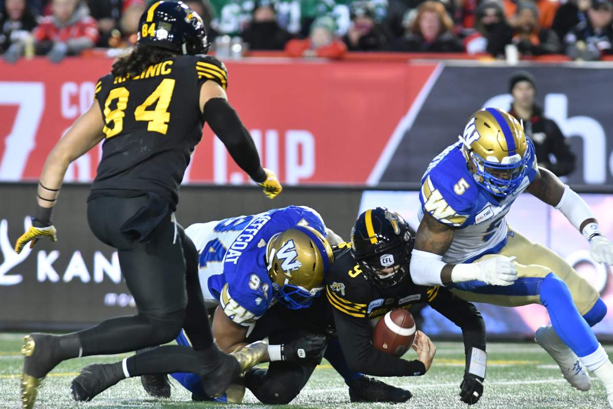 Hamilton Tiger-Cats Dane Evans holds on to the ball as he is tackled by Winnipeg Blue Bombers Jackson Jeffcoat during the 1st quarter of CFL Grey Cup game action in Calgary Sunday. (CFL PHOTO – Walter Tychnowicz)