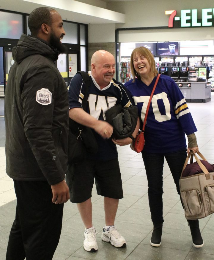 Chris Matthew and Darla Robinson are greeted at Calgary International Airport by Saskatchewan Roughrider and Team Shaw member, Manny Arceneaux. Shaw Communications invited the pair to attend the 107th Grey Cup after learning that Matthew vowed 18 years ago not to wear pants until the Winnipeg Blue Bombers win the Grey Cup.