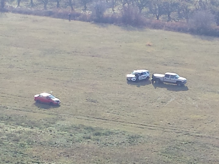 Two police vehicles are parked near what appears to be a suspicious vehicle in a Kelowna field.