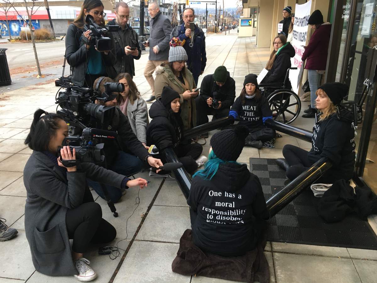 Media is seen interviewing protesters, who have chained themselves to a Kelowna building Monday morning.