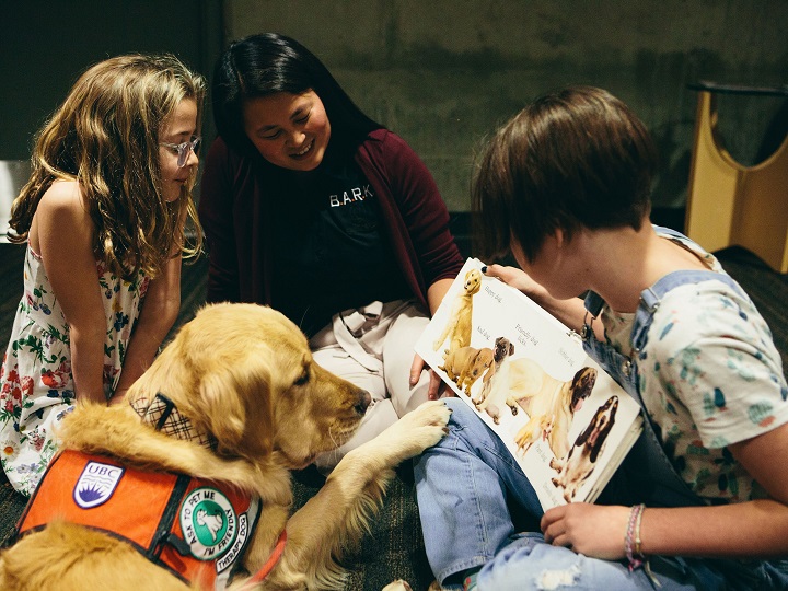 Golden retriever Abby listens while Annie Letheman, right, reads to her sister Ruby, with researcher Camille Rousseau, middle, observing.