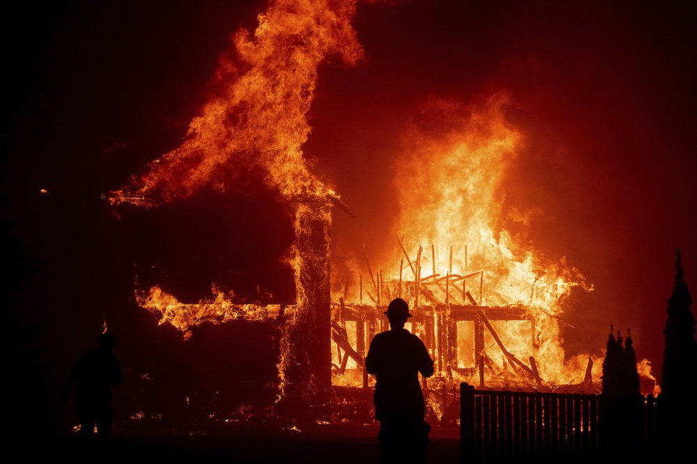 FILE - In this Nov. 8, 2018 file photo, a home burns as a wildfire called the Camp Fire rages through Paradise, Calif. Pacific Gas and Electric says it has reached a $13.5 billion settlement that will resolve all major claims related to devastating wildfires blamed on its outdated equipment and negligence. The settlement, which the utility says was reached Friday, Dec. 6, 2019, still requires court approval. 