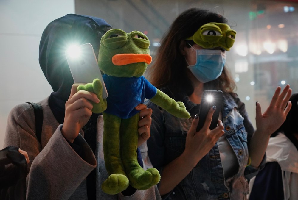 People raise their cellphones lights and stuffed frog toy as they form a human chain on New Year’s eve in Hong Kong, Tuesday, Dec. 31, 2019.