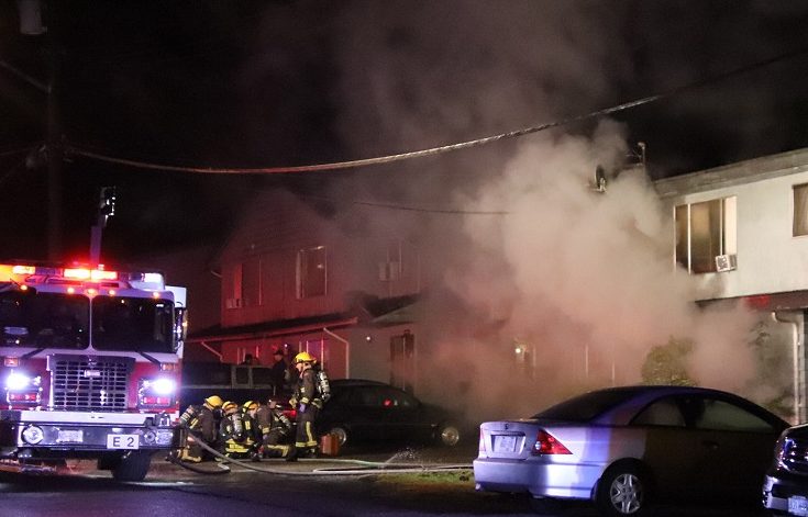 Firefighters attend to a rescued person as heavy smoke pours out of a Surrey four-plex on Dec. 22, 2019.