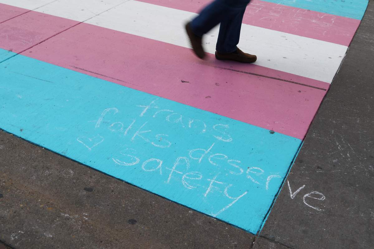 A person walks on a trans Pride flag crosswalk in Calgary on Aug. 18, 2019. The flag was defaced with a violent message but later covered with fresh paint. Positive messages were left written with chalk.