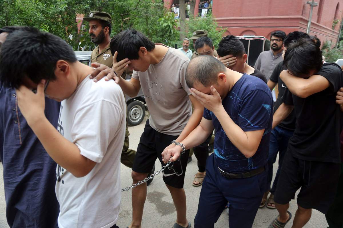 In this May 11, 2019 photo, detained Chinese nationals, accused of involvement in a trafficking gang to lure Pakistani women into fake marriages, try to shield their faces while they are escorted by Pakistan\’s Federal Investigation Agency officers to court in Lahore, Pakistan.