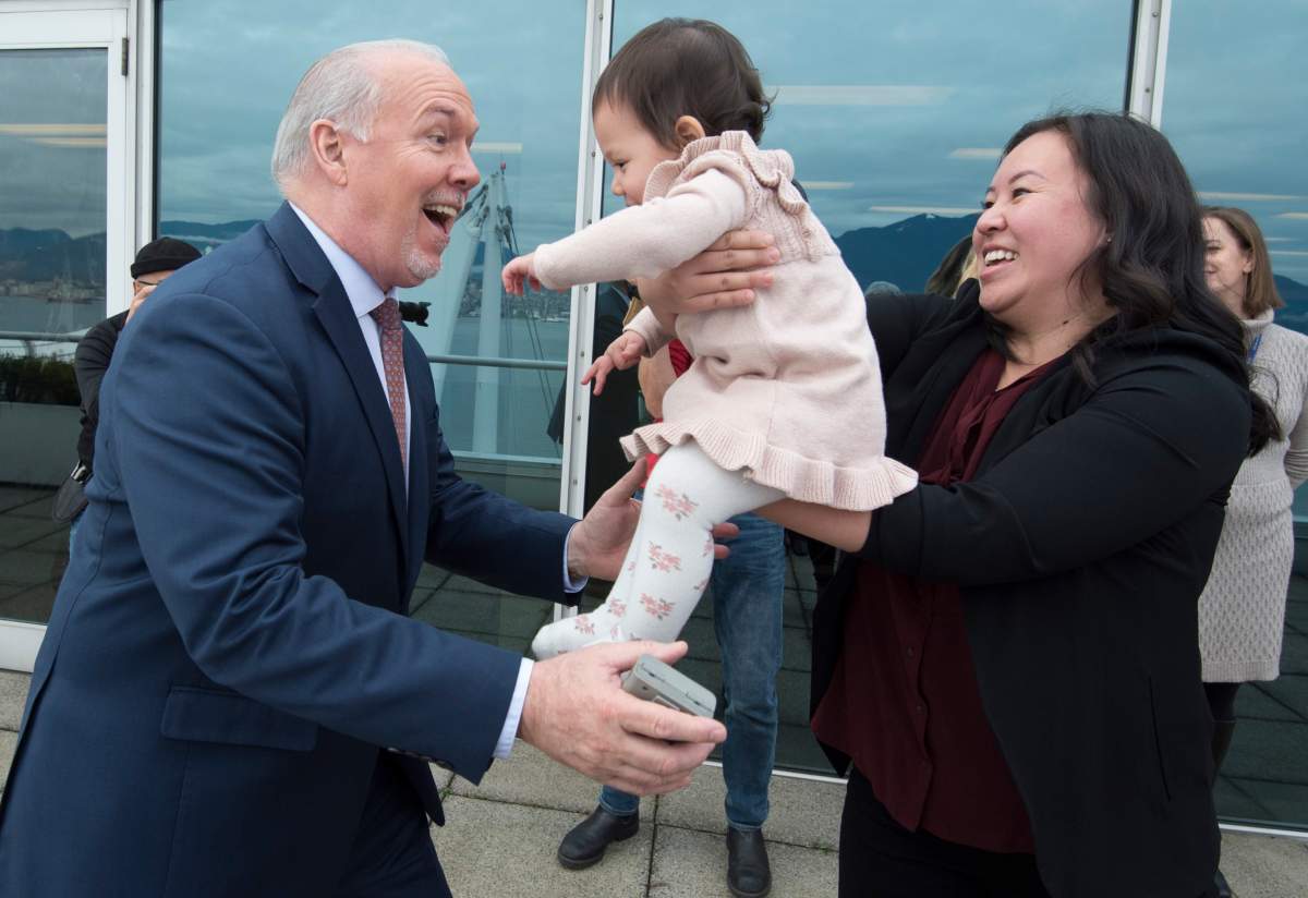 British Columbia Premier John Horgan pretends to catch Thirteen-month-old Caliah Kornneluk from her mom Jocye Yan after the premier along with Minister of Finance, Carole James and Minister of Health, Adrian Dix held a news conference in downtown Vancouver., Thursday, December, 5, 2019. The Premier and the Ministers announced that they are stopping the Medical Services Plan premiums (MSP) in the province.