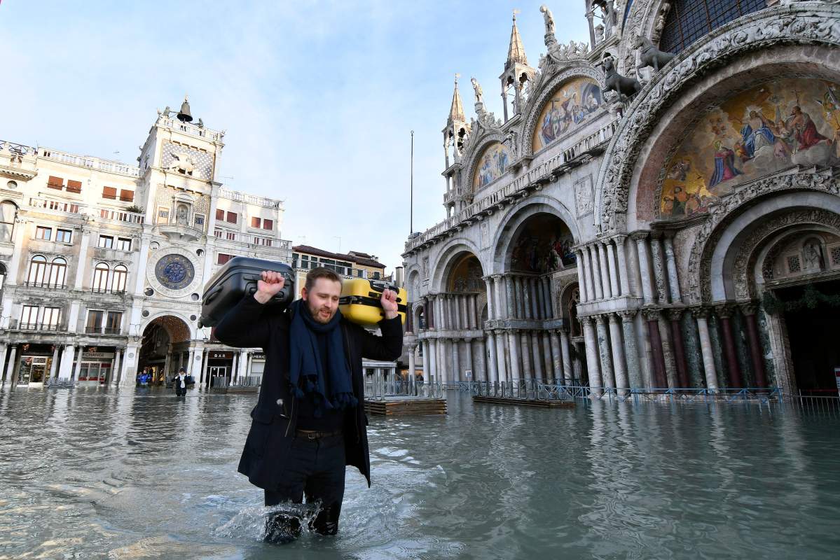 A man carries suitcases as he wades through water during a high tide of 1.44 meters (4.72 feet), in St. Mark’s Square, in Venice, Italy, Monday, Dec. 23, 2019.