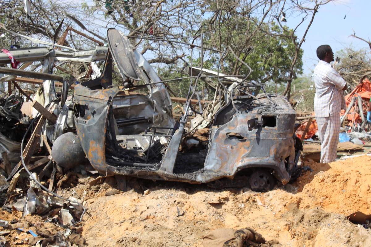 A man stands next to a destroyed vehicle at the scene of a large explosion near a check point in Mogadishu, Somalia, 28 December 2019.