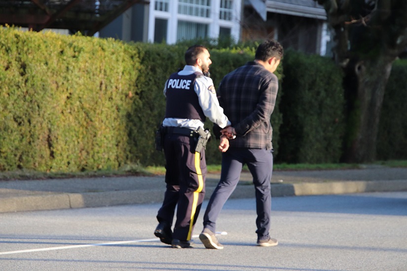 A man is led in handcuffs away from the scene of a serious crash in Burnaby on Dec. 25, 2019.