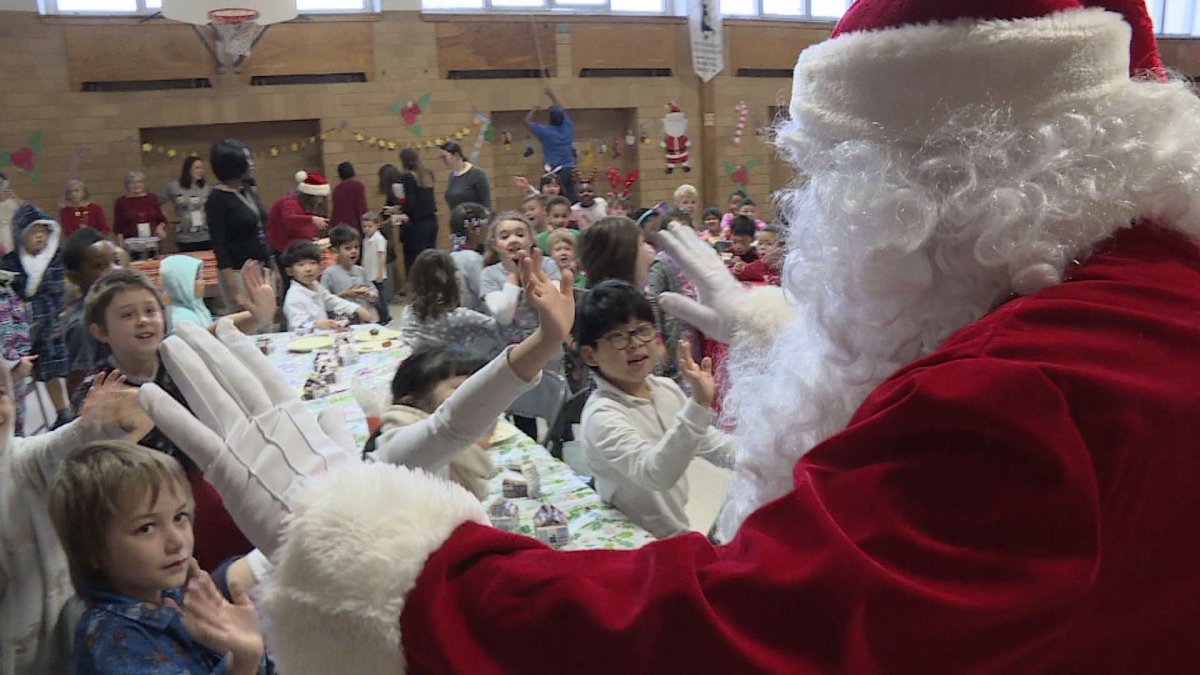 Someone dressed as Santa Claus enters an auditorium at Saint Monica Elementary School for the Generations Foundation's Breakfast with Santa and gift giveaway.