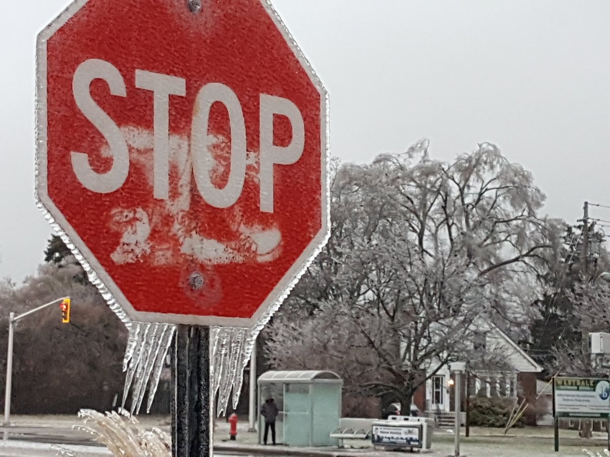 Icicles hang from a stop sign that sits in the foreground of a wintry scene.