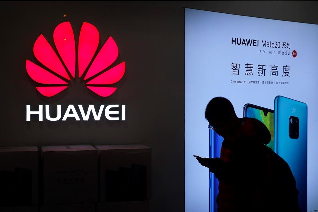 In this Dec. 11, 2018, photo, a man browses his smartphone outside a Huawei store at a shopping mall in Beijing. (AP Photo/Andy Wong).