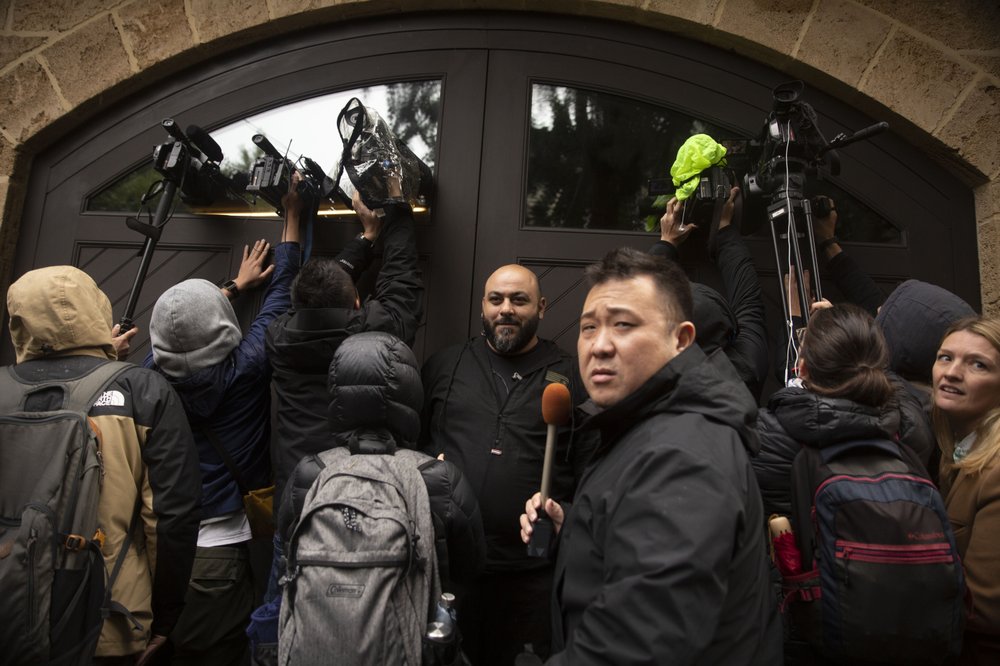 A private security guard, center, stands as journalists film through the garage window of the home of former Nissan Chairman Carlos Ghosn in Beirut, Lebanon, Thursday, Jan. 2, 2020.