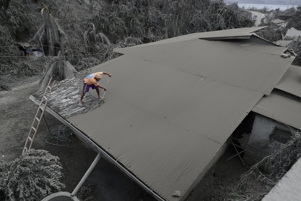 A resident clears volcanic ash from his roof in Laurel, Batangas province, southern Philippines on Tuesday, Jan. 14, 2020. Taal volcano is spewing ash half a mile high and trembling with earthquakes constantly as thousands of people flee villages darkened and blanketed by heavy ash.