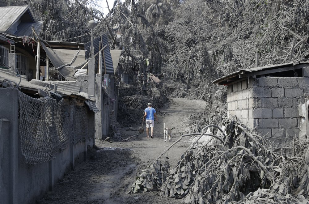 A resident walks past structures and trees damaged by volcanic ash at Laurel, Batangas province, southern Philippines on Tuesday, Jan. 14, 2020. Taal volcano is spewing ash half a mile high and trembling with earthquakes constantly as thousands of people flee villages darkened and blanketed by heavy ash.