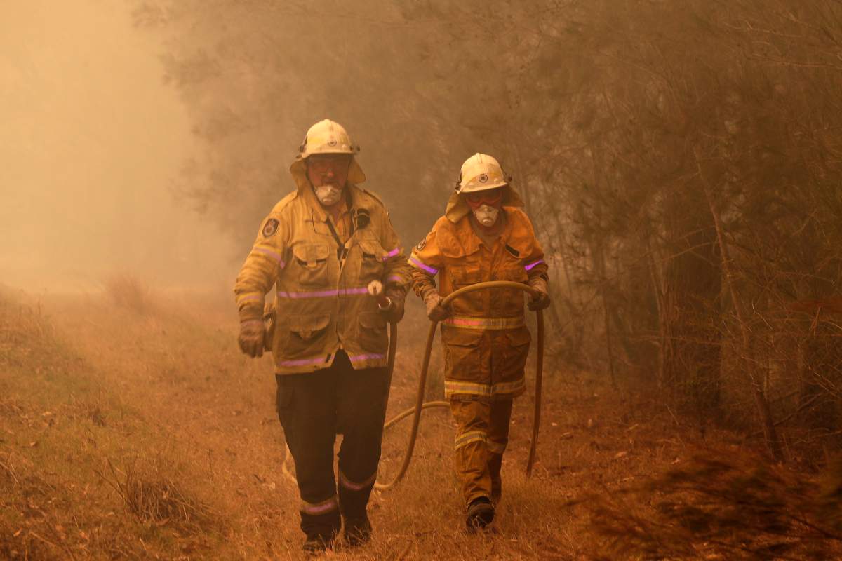 Firefighters drag their water hose after putting out a spot fire near Moruya, Australia, Jan. 4, 2020.