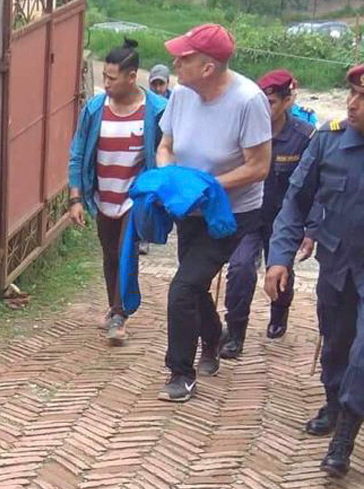 In this July 8, 2019 photo, Canadian aid worker Peter Dalglish, centre wearing red cap, is brought to appear before the Kavre District Court in Nepal.