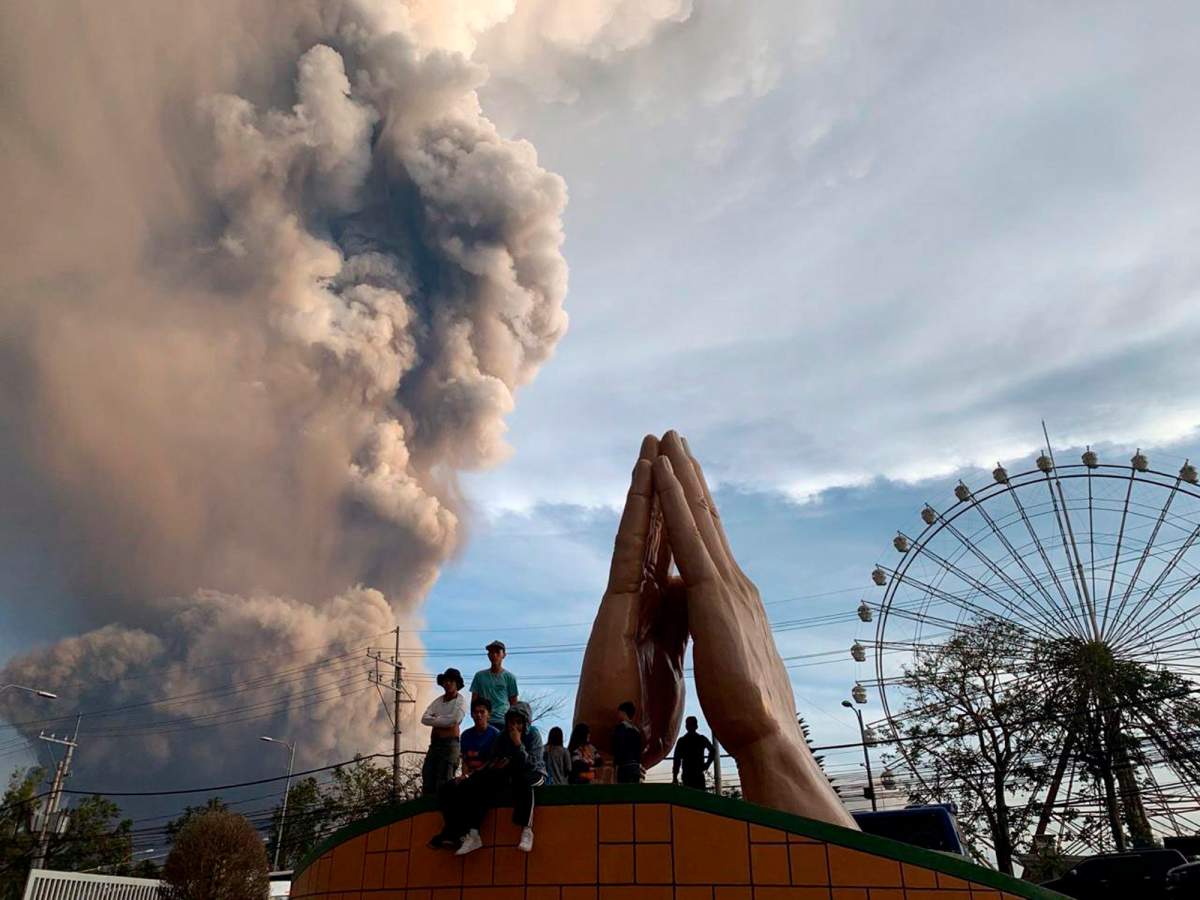 In this Sunday, Jan. 12, 2020, photo, people watch as the Taal volcano spews ash and smoke during an eruption in Tagaytay, Cavite province south of Manila, Philippines.