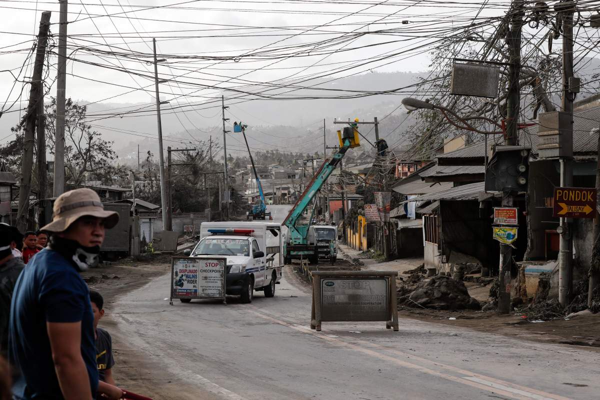 Workers remove ash from electrical posts at a checkpoint following the eruption of Taal Volcano in Talisay, Batangas, Philippines, 15 January 2020.