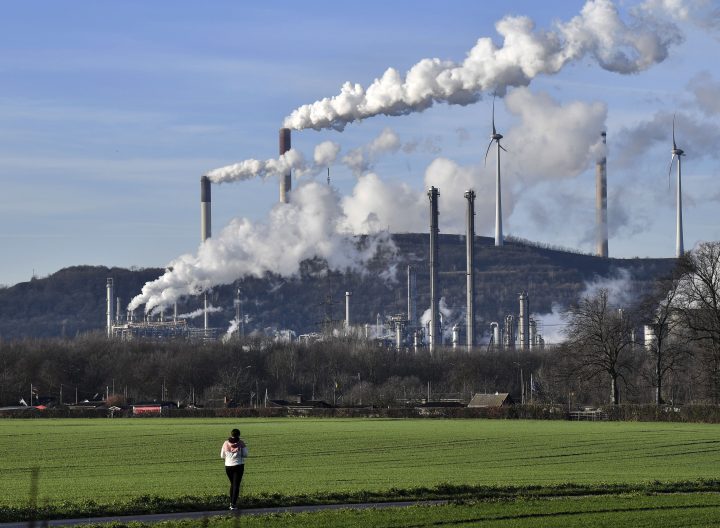 A woman walks in front of a steaming Uniper coal-fired power plant and a BP refinery in Gelsenkirchen, Germany, Thursday, Jan. 16, 2020. 