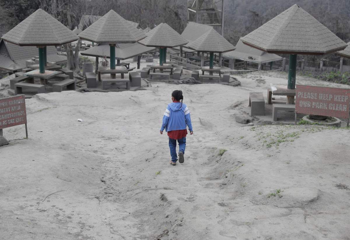 A woman walks along a park covered in volcanic-ash at a town near Taal volcano in Tagaytay, Cavite province, southern Philippines on Sunday Jan. 19, 2020.