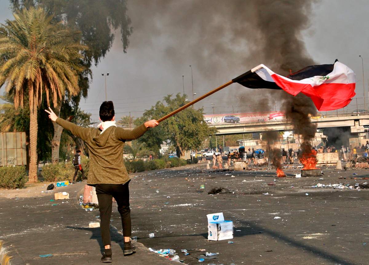 A protester waves the national flag during clashes with security forces in central Baghdad, Iraq, Monday, Jan. 20, 2020. 