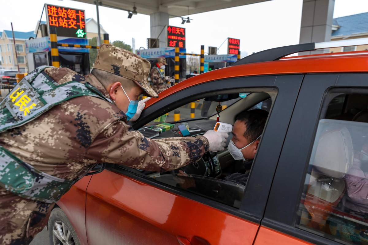 A militia member uses a digital thermometer to take a driver’s temperature at a checkpoint at a highway toll gate in Wuhan in central China’s Hubei Province, Thursday, Jan. 23, 2020.